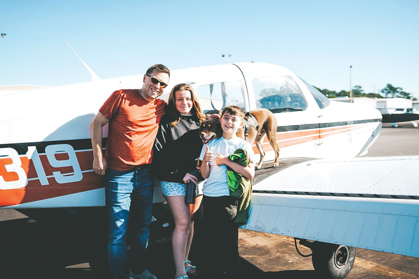People and a dog next to an airplane.