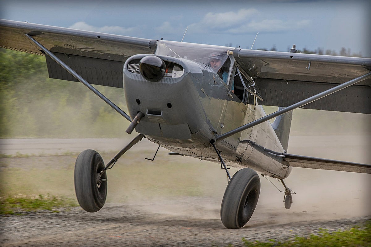 An airplane lands on a dirt strip in the backcountry