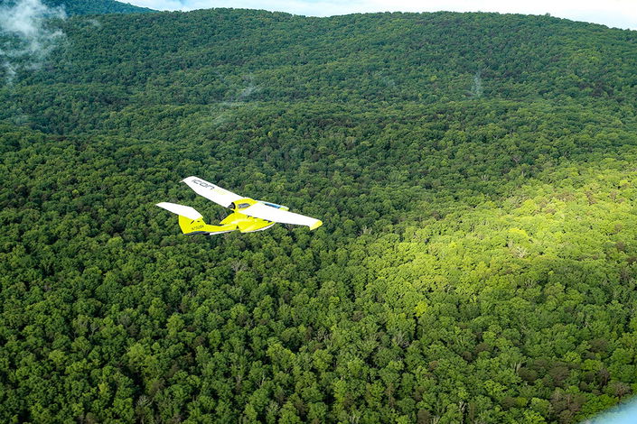 An Icon A5 aircraft flies over the treetops along the Sequatchie Valley.