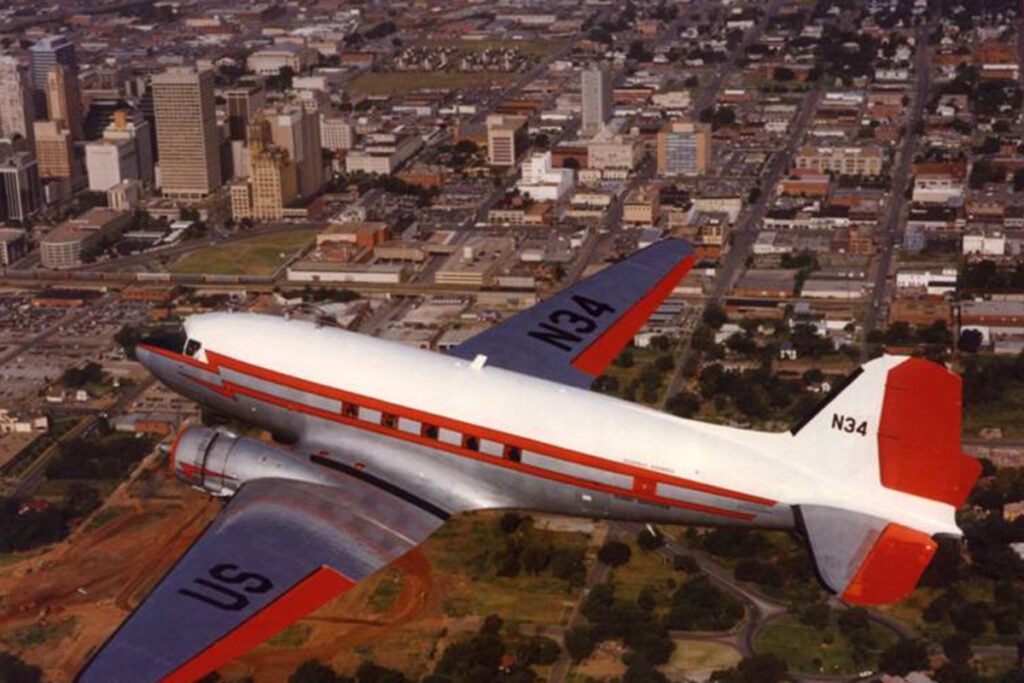 A DC-3 soars the skies over a city