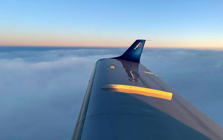 The wing and wingtip of a TBM 940 aircraft with a bed of clouds below and the horizon in the distance
